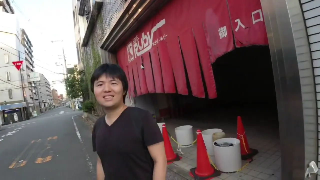 KC standing on a Japanese street outside a building with red entrance curtains