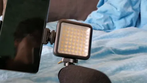 A phone mounted beside a small light panel and a foam-covered microphone.